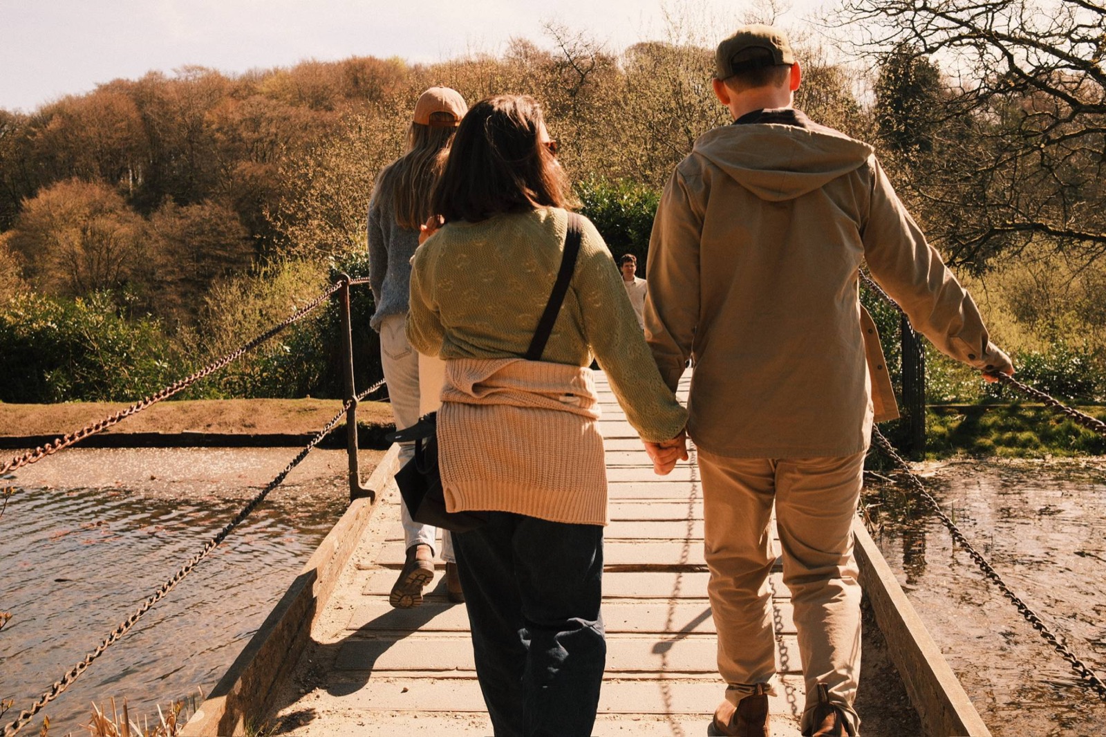 Friends walking hand in hand across a footbridge in spring